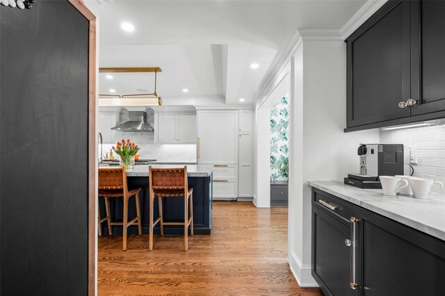 kitchen with decorative backsplash, wall chimney range hood, a kitchen bar, recessed lighting, and light wood finished floors