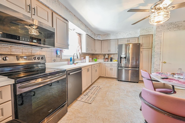 kitchen featuring a sink, wallpapered walls, light countertops, a ceiling fan, and appliances with stainless steel finishes