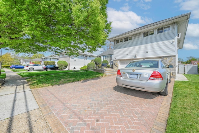 view of front of house featuring fence, stone siding, a garage, a front yard, and decorative driveway