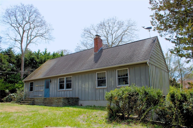 exterior space featuring roof with shingles, a chimney, board and batten siding, and a yard