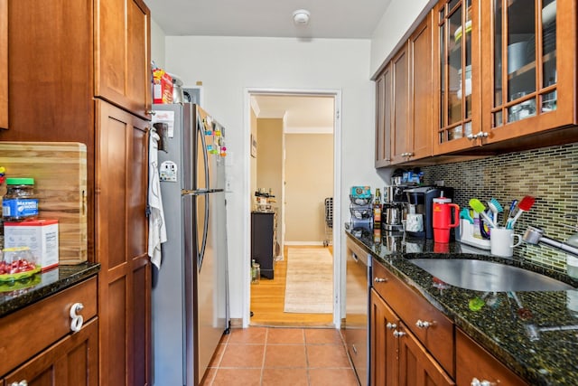 200 N Village Ave Unit D10, Rockville Centre, NY 11570 - kitchen featuring appliances with stainless steel finishes, brown cabinetry, dark stone countertops, backsplash, and glass insert cabinets