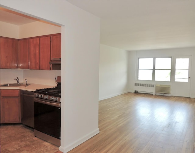 kitchen with a sink, radiator heating unit, under cabinet range hood, light countertops, and appliances with stainless steel finishes