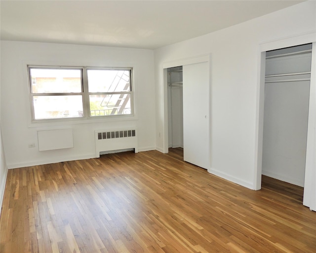 unfurnished bedroom featuring radiator, multiple windows, two closets, and light wood finished floors