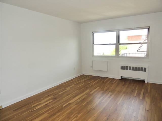 empty room with dark wood-style flooring, baseboards, and radiator heating unit