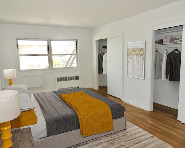 bedroom with baseboards, radiator, multiple closets, and wood finished floors