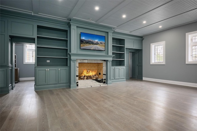 unfurnished living room with baseboards, built in features, wood finished floors, and a warm lit fireplace