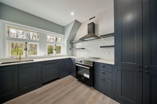 kitchen with wall chimney range hood, stainless steel electric range oven, open shelves, a sink, and light wood-style flooring