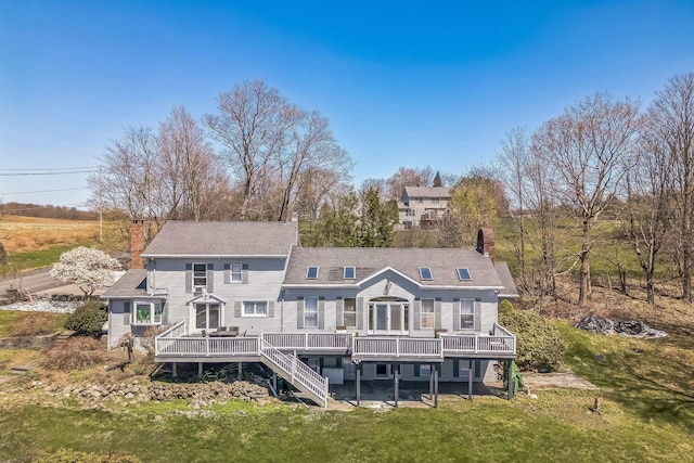 back of property with roof with shingles, a wooden deck, a chimney, and a yard