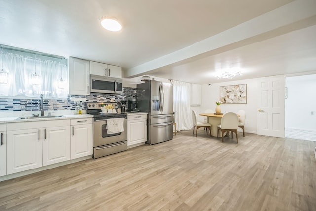 kitchen with appliances with stainless steel finishes, a sink, light wood-style floors, light countertops, and backsplash