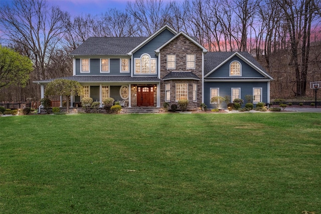view of front of house with a porch, a front yard, stone siding, and a shingled roof