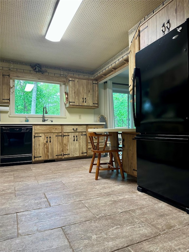 kitchen with light countertops, brown cabinetry, a sink, and black appliances