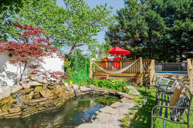 view of yard featuring a garden pond, a wooden deck, and a swimming pool
