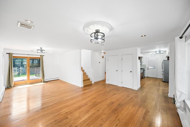 unfurnished living room featuring visible vents, baseboard heating, an inviting chandelier, light wood-type flooring, and stairs