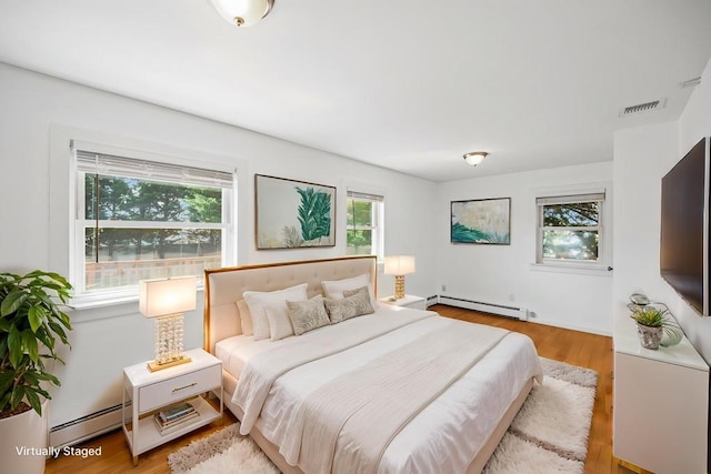 bedroom with a baseboard heating unit, visible vents, baseboard heating, and wood finished floors