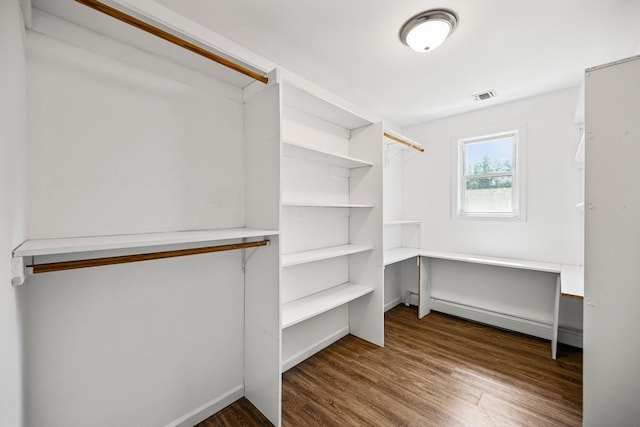spacious closet with baseboard heating, visible vents, and wood finished floors