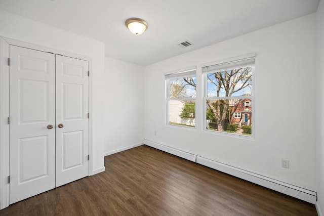 unfurnished bedroom featuring a baseboard heating unit, a closet, baseboards, visible vents, and dark wood-type flooring