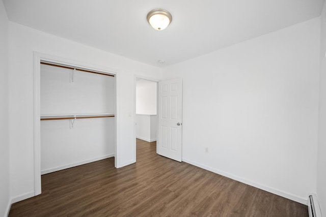 unfurnished bedroom with baseboards, a baseboard heating unit, dark wood-style flooring, and a closet
