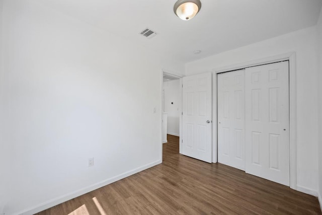 unfurnished bedroom featuring wood finished floors, visible vents, a closet, and baseboards