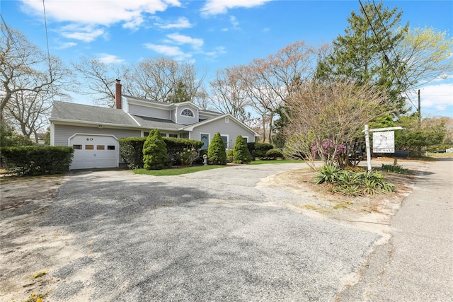 view of front facade featuring an attached garage, driveway, a chimney, and roof with shingles