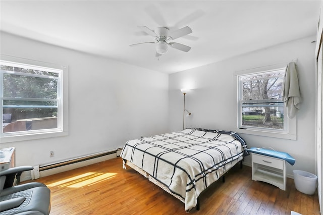 bedroom with ceiling fan, a baseboard heating unit, and hardwood / wood-style flooring