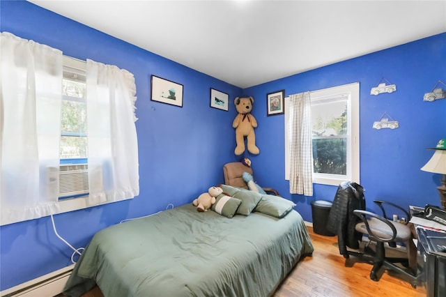 bedroom featuring wood finished floors, a baseboard heating unit, and multiple windows