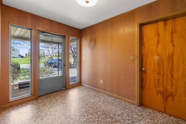 doorway to outside with tile patterned floors, wood walls, and baseboards