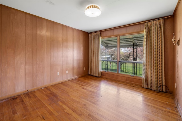 unfurnished room with baseboards, wooden walls, and hardwood / wood-style floors