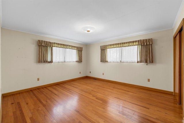 empty room with baseboards, ornamental molding, and light wood-style floors