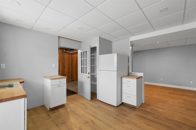 kitchen with freestanding refrigerator, butcher block countertops, a drop ceiling, and light wood-type flooring