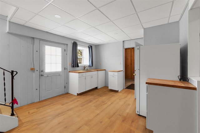 kitchen with a sink, white cabinets, wooden counters, and light wood-type flooring