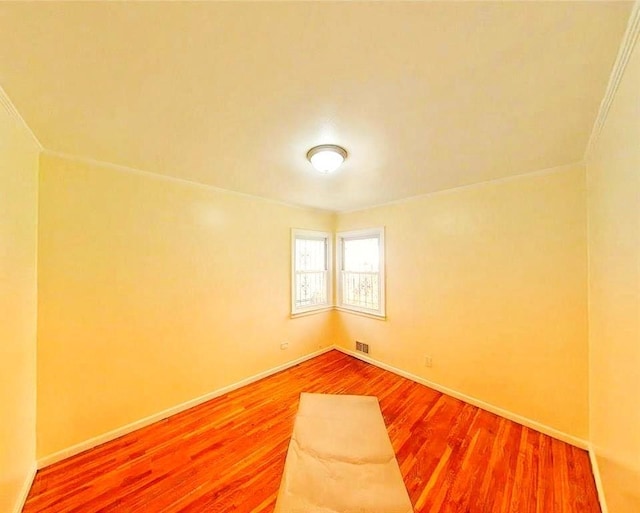 empty room with baseboards, visible vents, wood finished floors, and crown molding