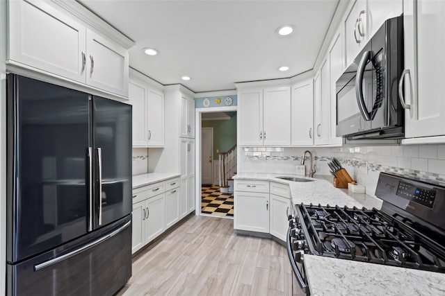 kitchen featuring a sink, light stone counters, white cabinets, and black appliances