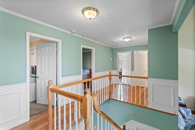 hallway with crown molding, wainscoting, wood finished floors, attic access, and an upstairs landing