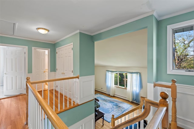corridor featuring crown molding, an upstairs landing, wainscoting, and light wood-style floors