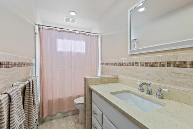 bathroom with visible vents, tile walls, vanity, toilet, and shower / tub combo with curtain