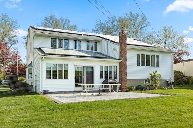 back of property with solar panels, a chimney, a lawn, a patio area, and fence