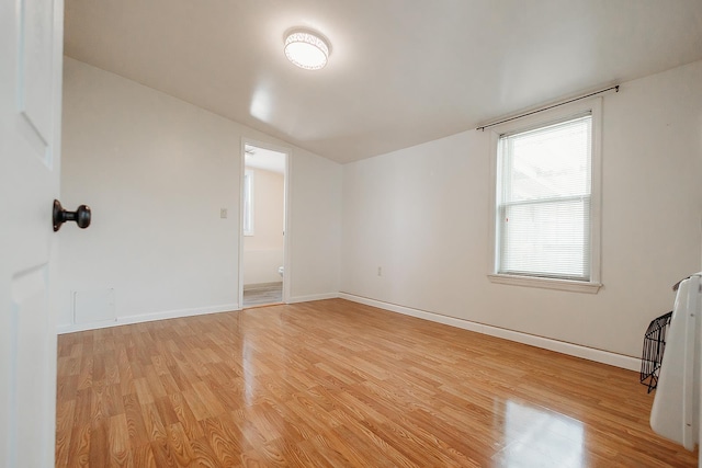 spare room with lofted ceiling, light wood-style flooring, and baseboards