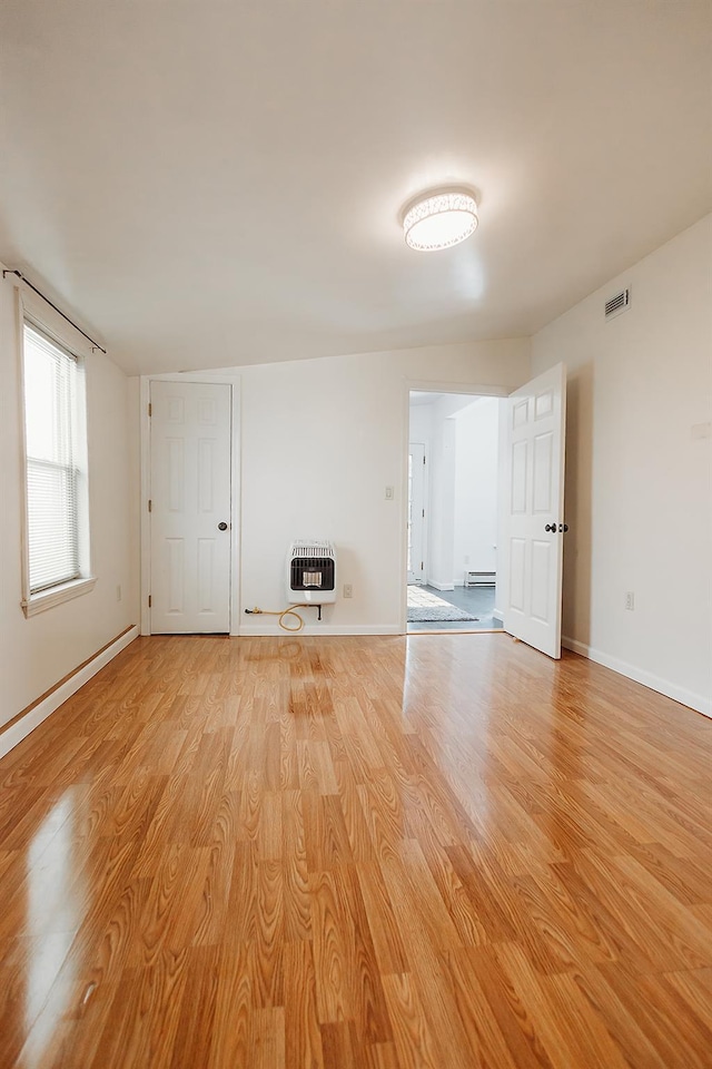 unfurnished living room with light wood finished floors, heating unit, visible vents, and baseboards