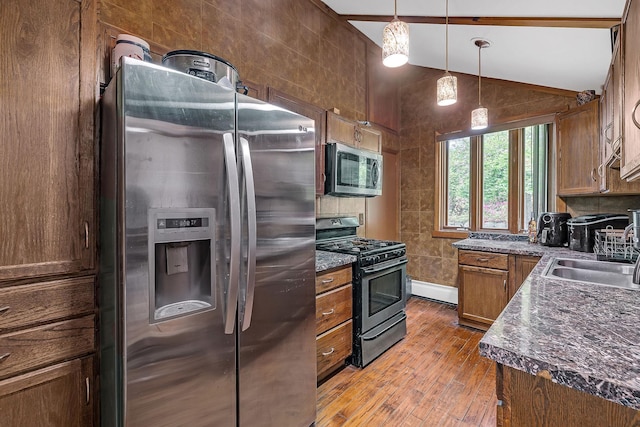 kitchen featuring appliances with stainless steel finishes, a sink, light wood-style flooring, lofted ceiling, and brown cabinetry