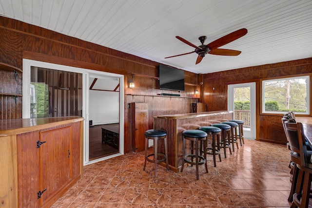 kitchen featuring wooden walls, ceiling fan, a kitchen breakfast bar, brown cabinets, and open shelves