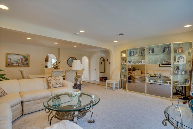 carpeted living room with arched walkways, recessed lighting, and visible vents