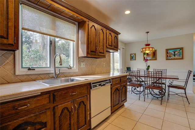 kitchen featuring white dishwasher, a sink, decorative light fixtures, light tile patterned floors, and backsplash