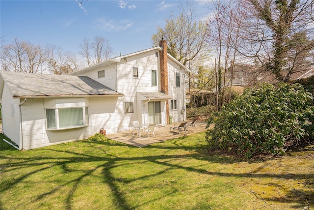 rear view of house with a patio, a shingled roof, a lawn, and a chimney