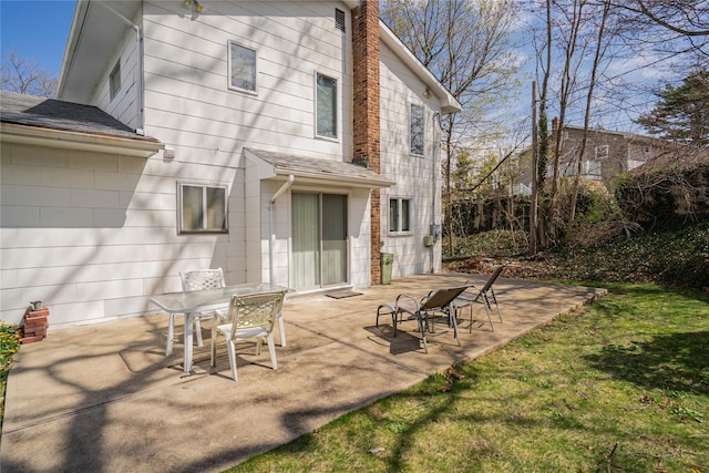 rear view of property featuring a patio, outdoor dining area, roof with shingles, and a chimney