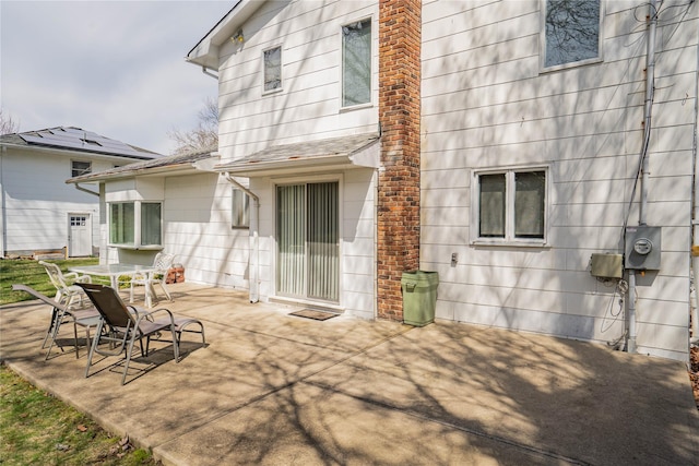 back of property with roof with shingles and a patio area