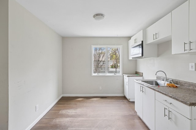 kitchen with light wood-type flooring, baseboards, white cabinets, and a sink