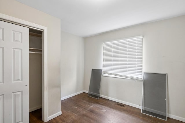 unfurnished bedroom featuring wood finished floors, visible vents, a closet, and baseboards