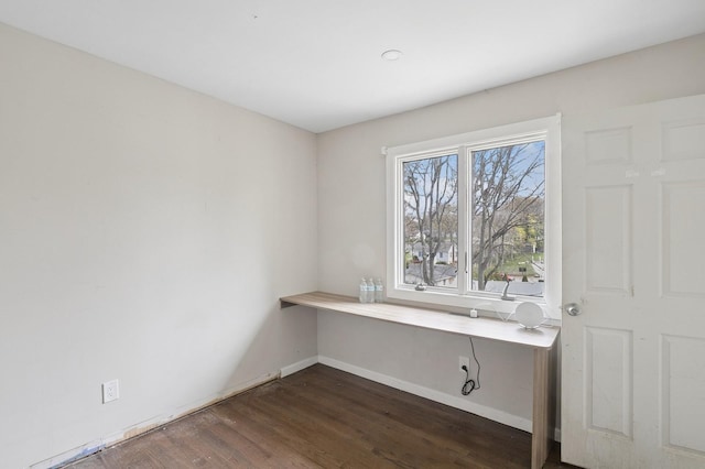 unfurnished office with dark wood finished floors, baseboards, and built in desk