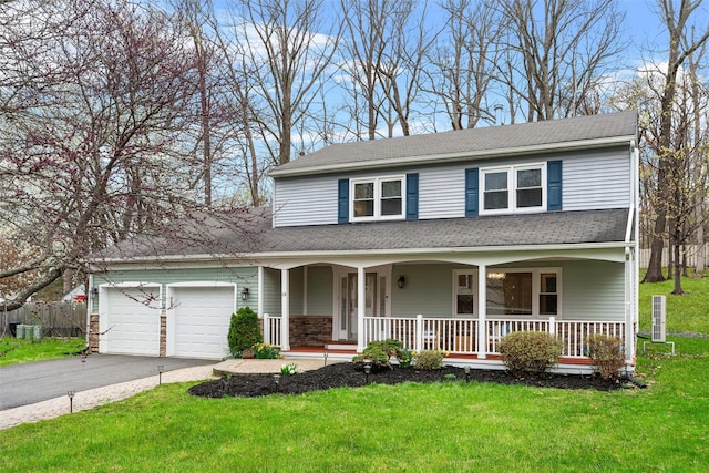traditional-style house with covered porch, roof with shingles, a front yard, aphalt driveway, and an attached garage