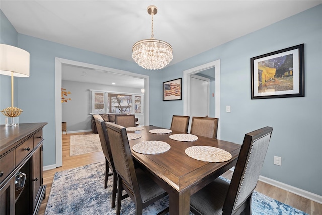 dining space featuring light wood-style floors, baseboards, and a notable chandelier